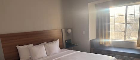 A neatly made bed with a wooden headboard, a bedside table with a lamp, and a window with curtains.