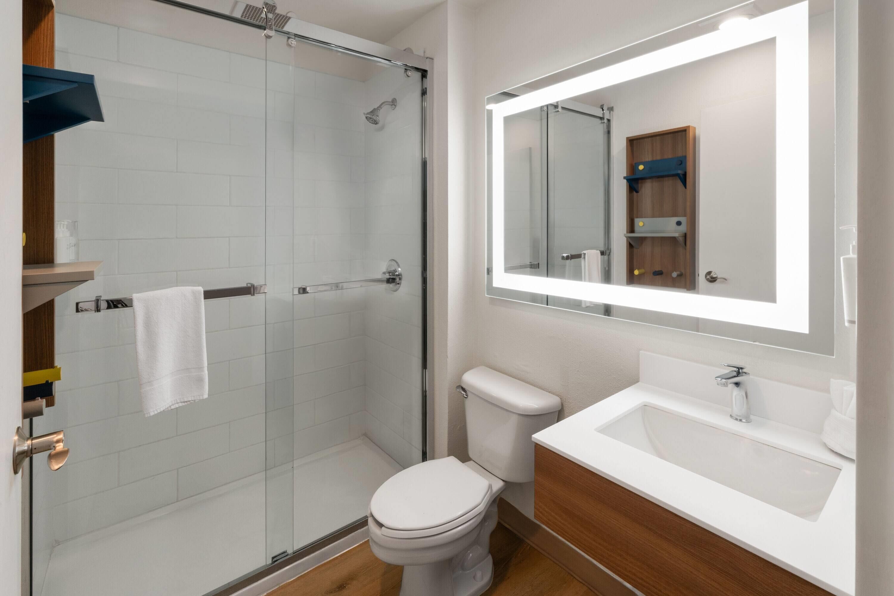 Un baño moderno con cabina de ducha de vidrio, inodoro blanco y tocador con espejo.
