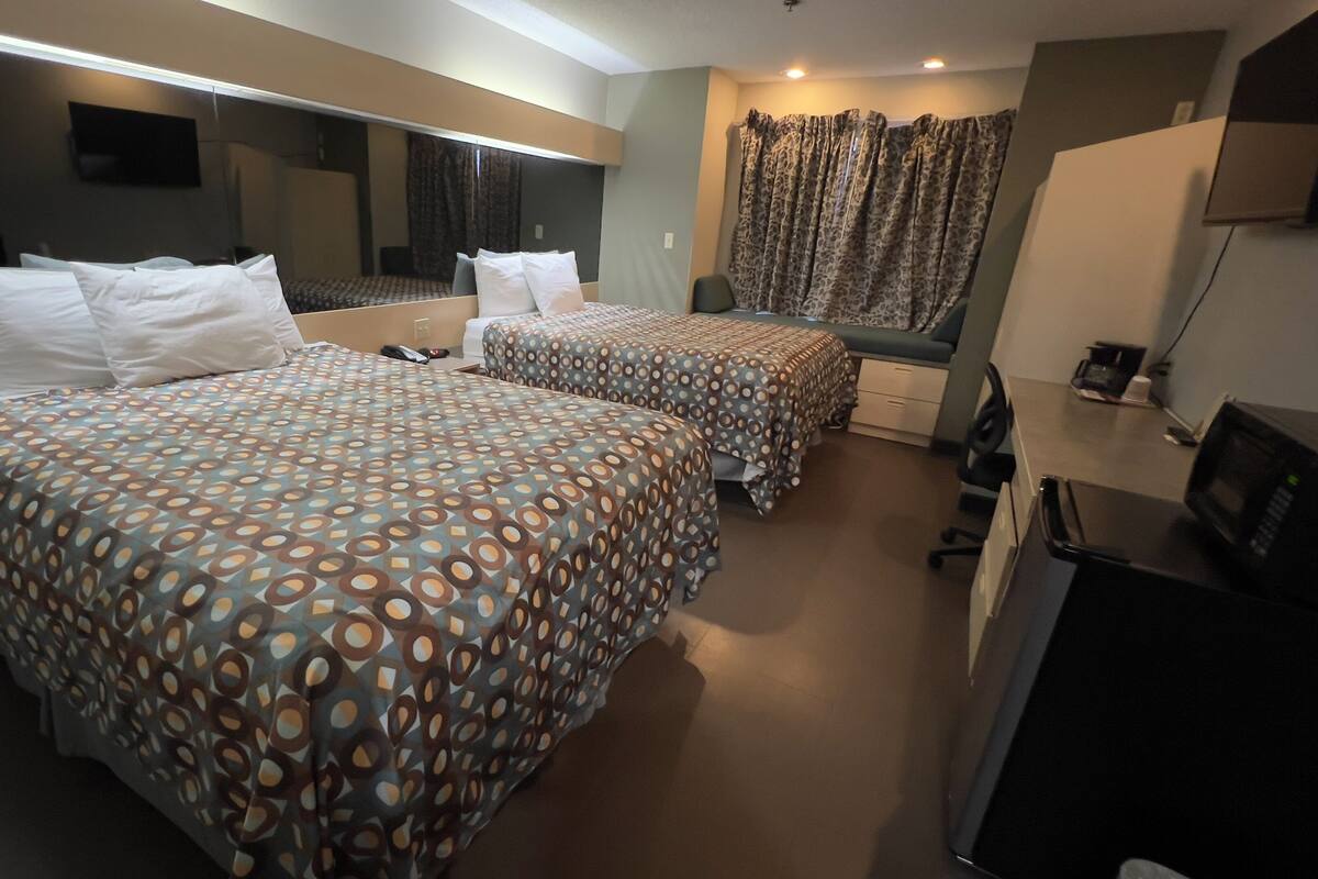 Ein Hotelzimmer mit zwei Betten, einem Schreibtisch, einem Fernseher und einem großen Spiegel.