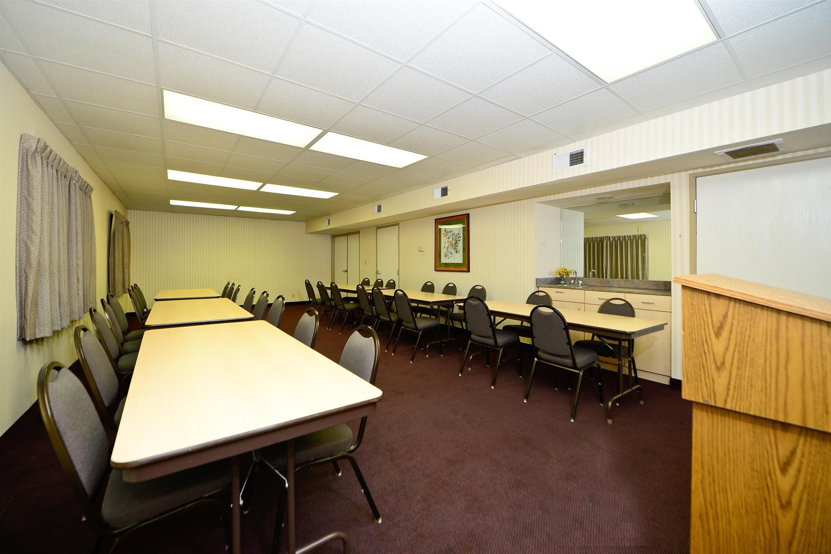 A conference room with a long table, multiple chairs, a wooden podium, and a large mirror on the wall.