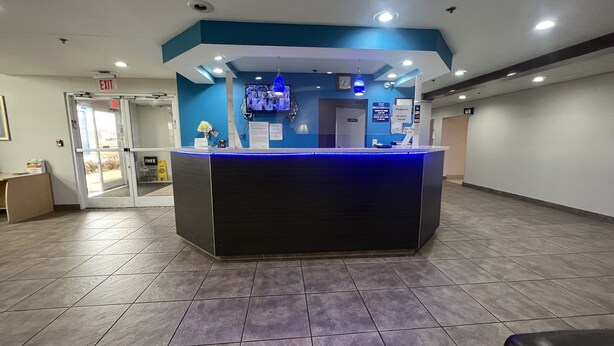 A reception desk with a blue and white color scheme, a glass door entrance, and a tiled floor. - Americas Best Value Inn & Suites Jackson, TN (Jackson)