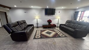 A living room with two leather sofas, a flat-screen TV, two floor lamps, and a patterned rug. - Americas Best Value Inn & Suites Jackson, TN (Jackson)
