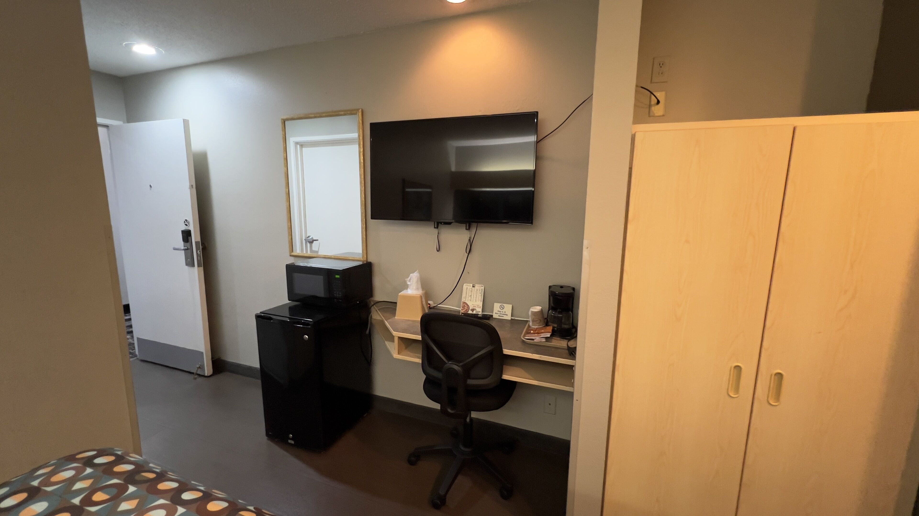 A hotel room with a bed, a desk with a computer, a TV, a microwave, and a wardrobe.