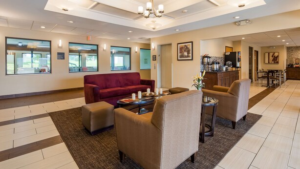 En hotellobby med en röd soffa, beige fåtöljer, ett soffbord och ett köksområde i bakgrunden.