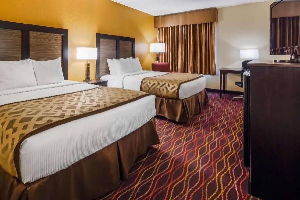 Une chambre d’hôtel avec deux lits, un bureau, une chaise et un grand miroir.