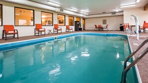 En inomhuspool med kristallklart blått vatten, omgiven av orangefärgade stolar och ett bord placerat vid poolkanten.
