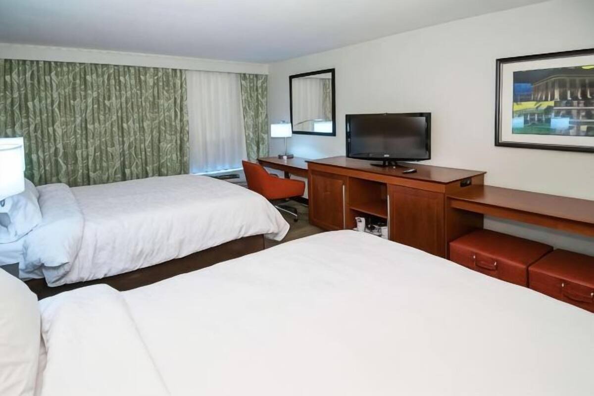 A hotel room with two beds, a desk with a television, a chair, and a red bench.