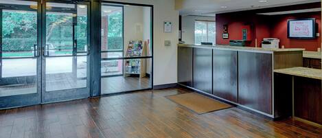 Un espace d’accueil doté d’un plancher en bois, d’un comptoir de réception et d’une porte en verre donnant sur l’extérieur.