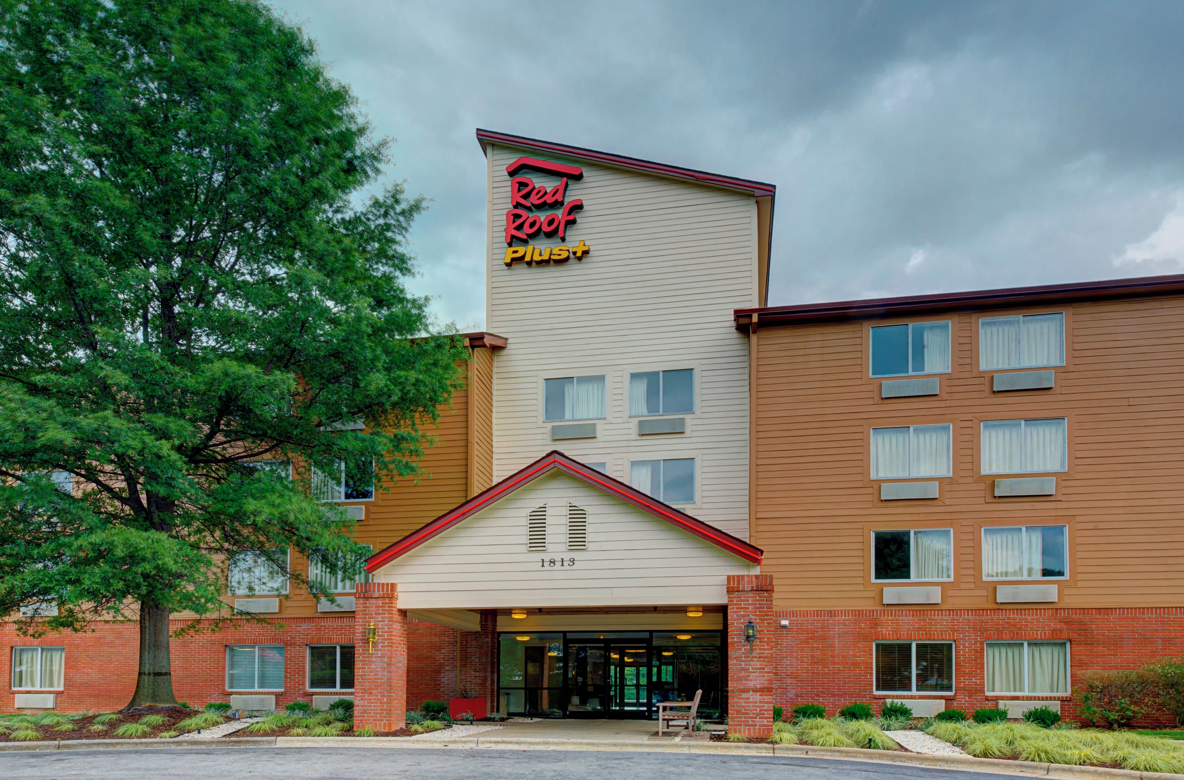 Ein Hotel mit auffälligem rot-gelb gestreiftem Schild, einer Ziegel-Fassade und einem großen Baum davor.