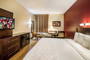 A hotel room with a bed, a desk, a television, a chair, a lamp, and a window with curtains. - Red Roof Inn PLUS+ Raleigh Downtown – NCSU/Conv Center (Raleigh)