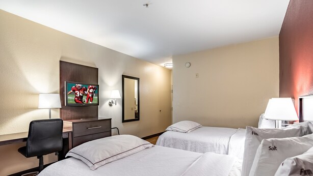Ein Hotelzimmer mit zwei Betten, einem Schreibtisch, einem Stuhl, einem Fernseher und einem Spiegel.