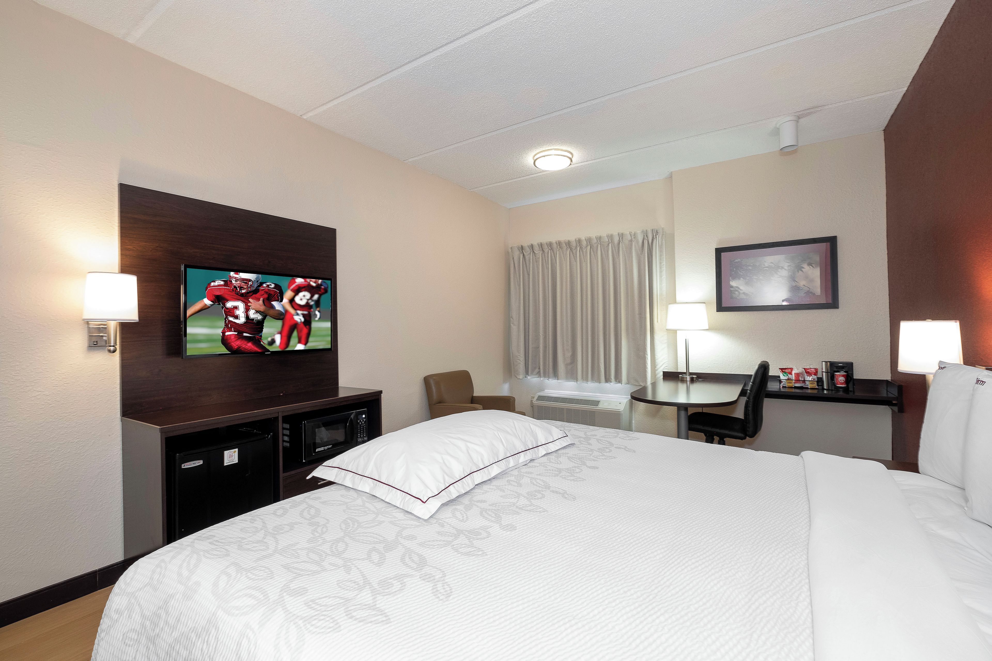A hotel room with a bed, a desk, a chair, a television, and a picture on the wall.