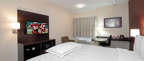 A hotel room with a bed, a desk, a chair, a television, and a picture on the wall.