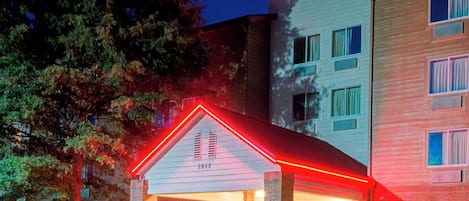 Hotel com fachada de tijolos, entrada coberta e placa de neon.