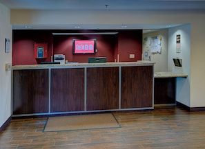 A reception desk with a digital display, a bulletin board, and a wooden floor. - Red Roof Inn PLUS+ Raleigh Downtown – NCSU/Conv Center (Raleigh)