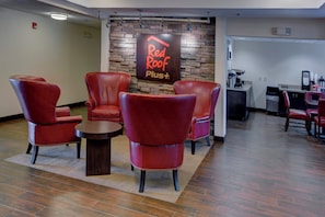 A Red Roof Plus lounge area with leather chairs, a coffee station, and a stone wall backdrop. - Red Roof Inn PLUS+ Raleigh Downtown – NCSU/Conv Center (Raleigh)