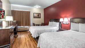 Ein Hotelzimmer mit zwei Betten, einem Schreibtisch mit Lampe, einem Sessel, einem Tisch und einem Bild an der Wand.