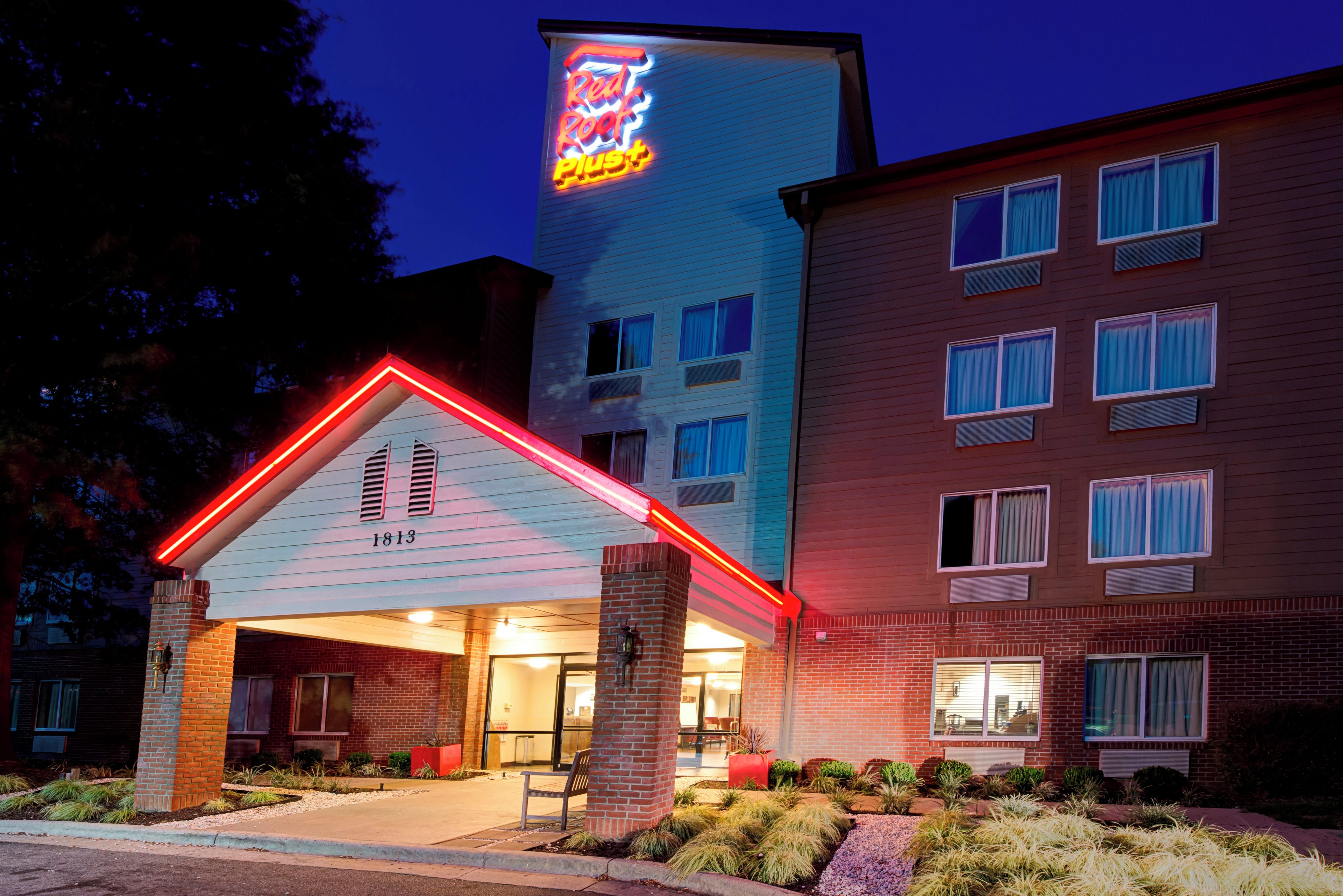 A hotel with a neon sign, a covered entrance, and a brick facade.