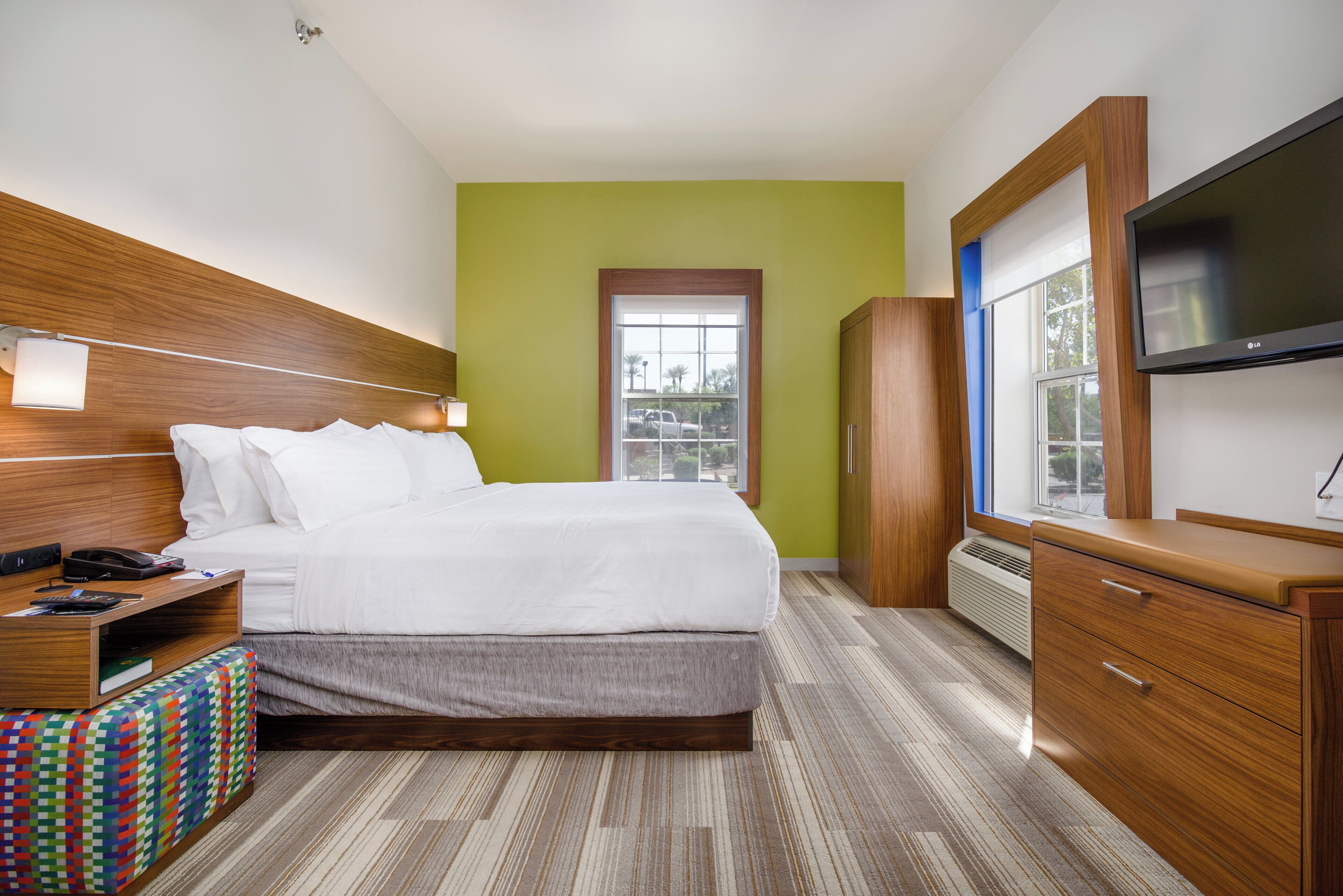 A hotel room with a bed, bedside table, TV, wardrobe, and a window.
