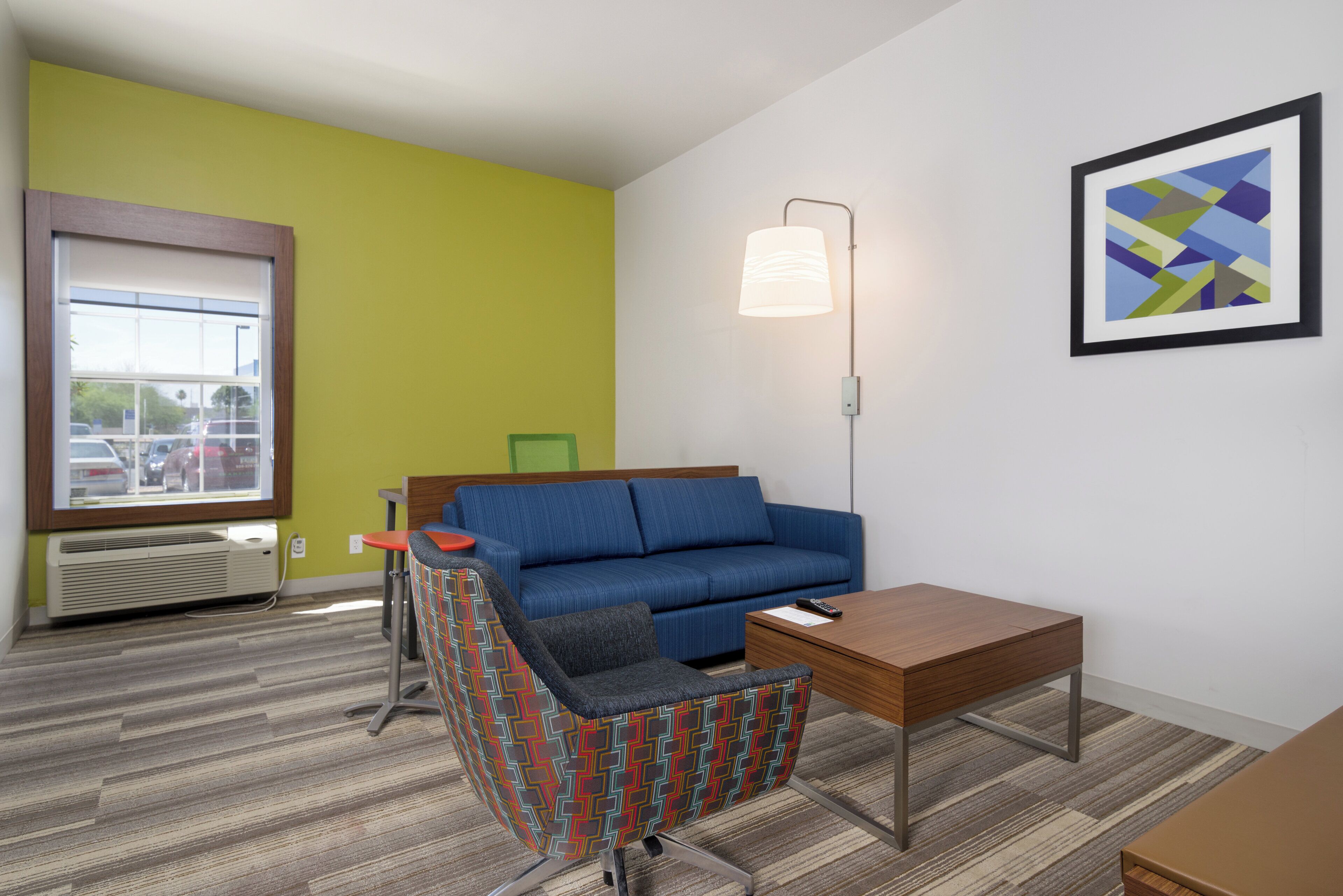 A room with a blue sofa, a patterned armchair, a wooden side table, a floor lamp, and a framed abstract painting on the wall.
