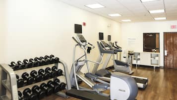 Une salle de sport équipée de tapis de course, de vélos elliptiques et d’une série de haltères.