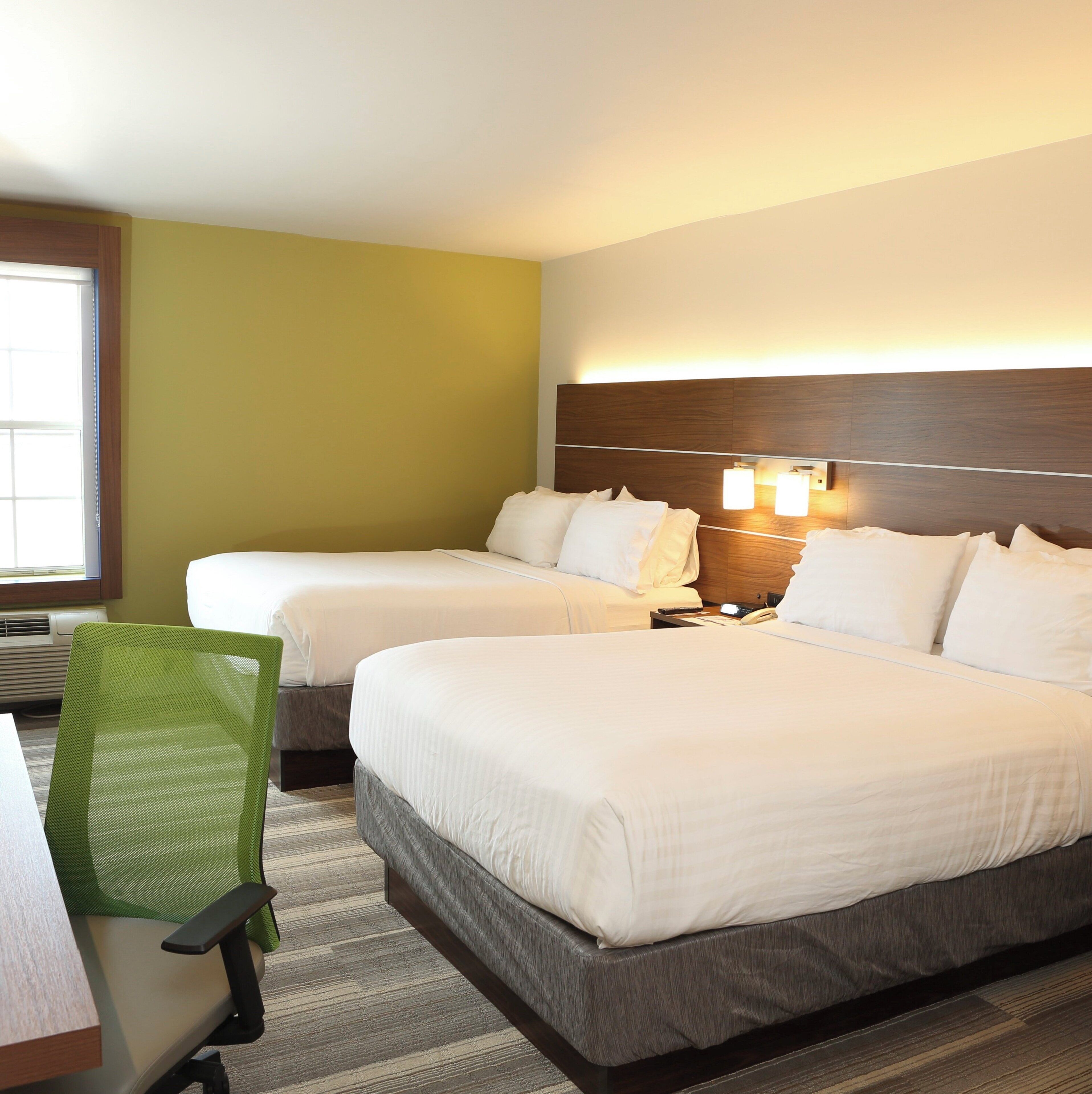 A hotel room with two beds, a desk, a chair, and a window.