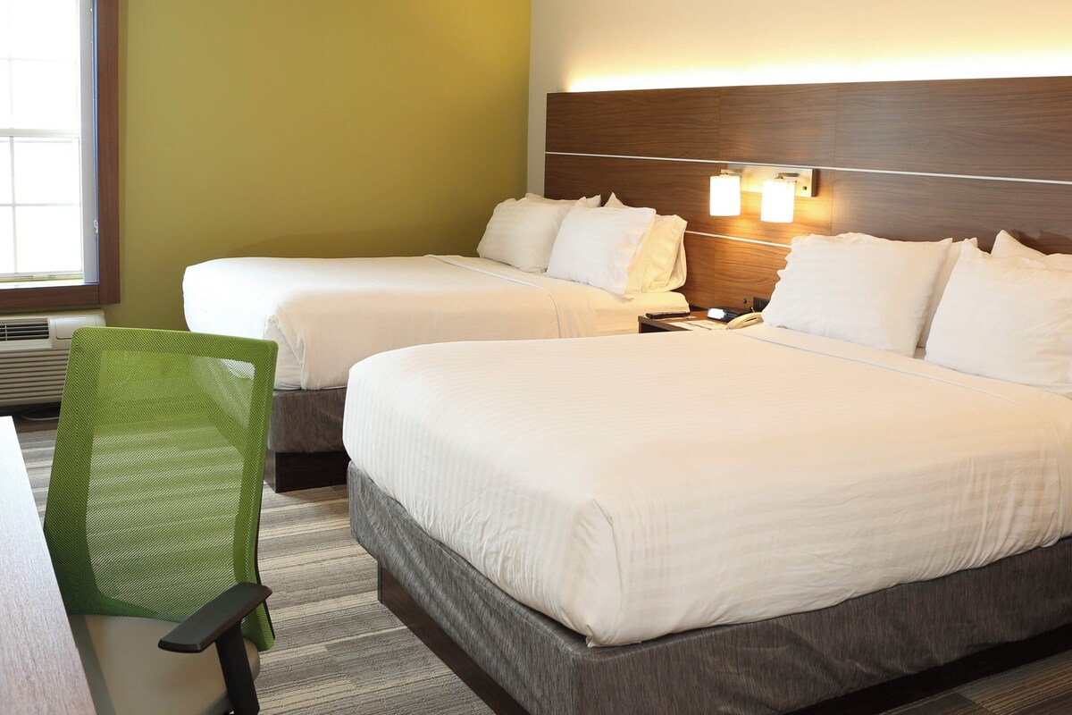 A hotel room with two beds, a desk, a chair, and a window.