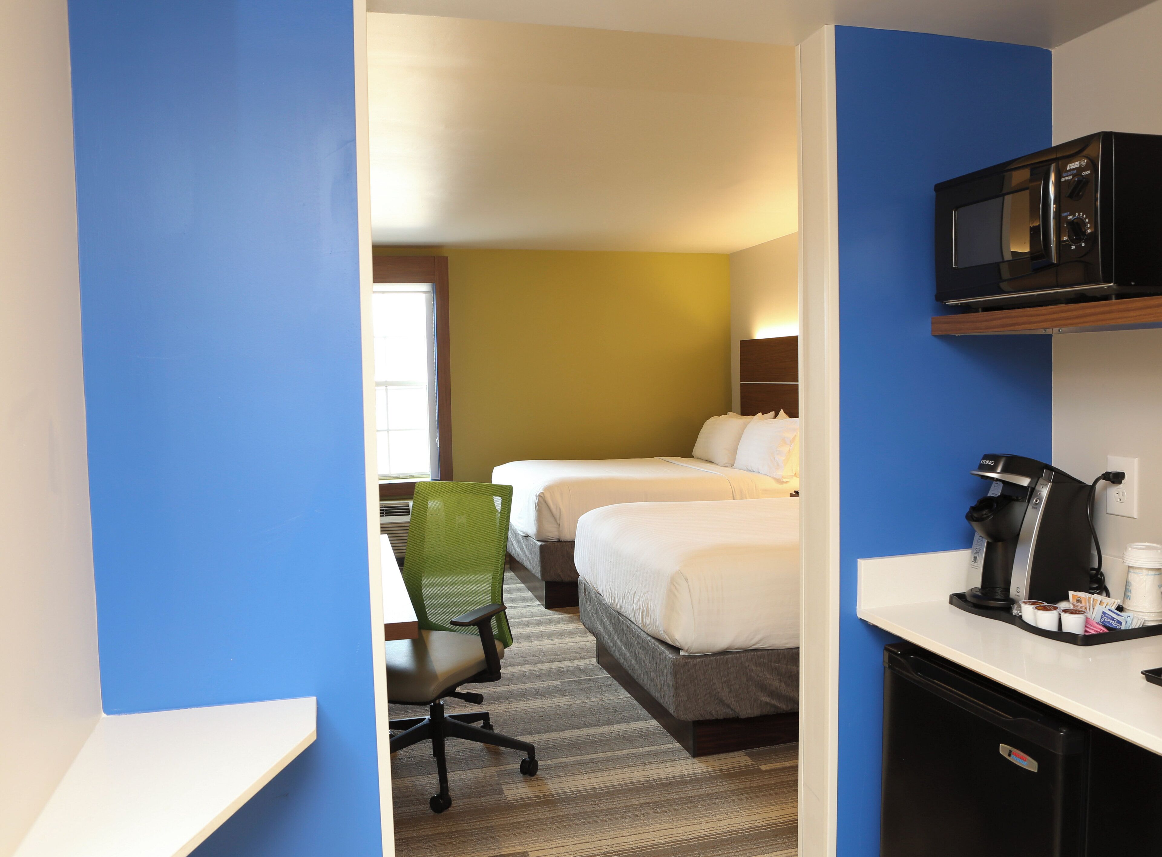 Une chambre d’hôtel équipée d’un bureau, d’un four à micro-ondes, d’une machine à café et de deux lits.
