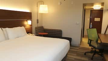 Una habitación de hotel con una cama grande, una mesita de noche con lámpara, una pequeña mesa redonda, una silla de oficina verde y un escritorio de madera.
