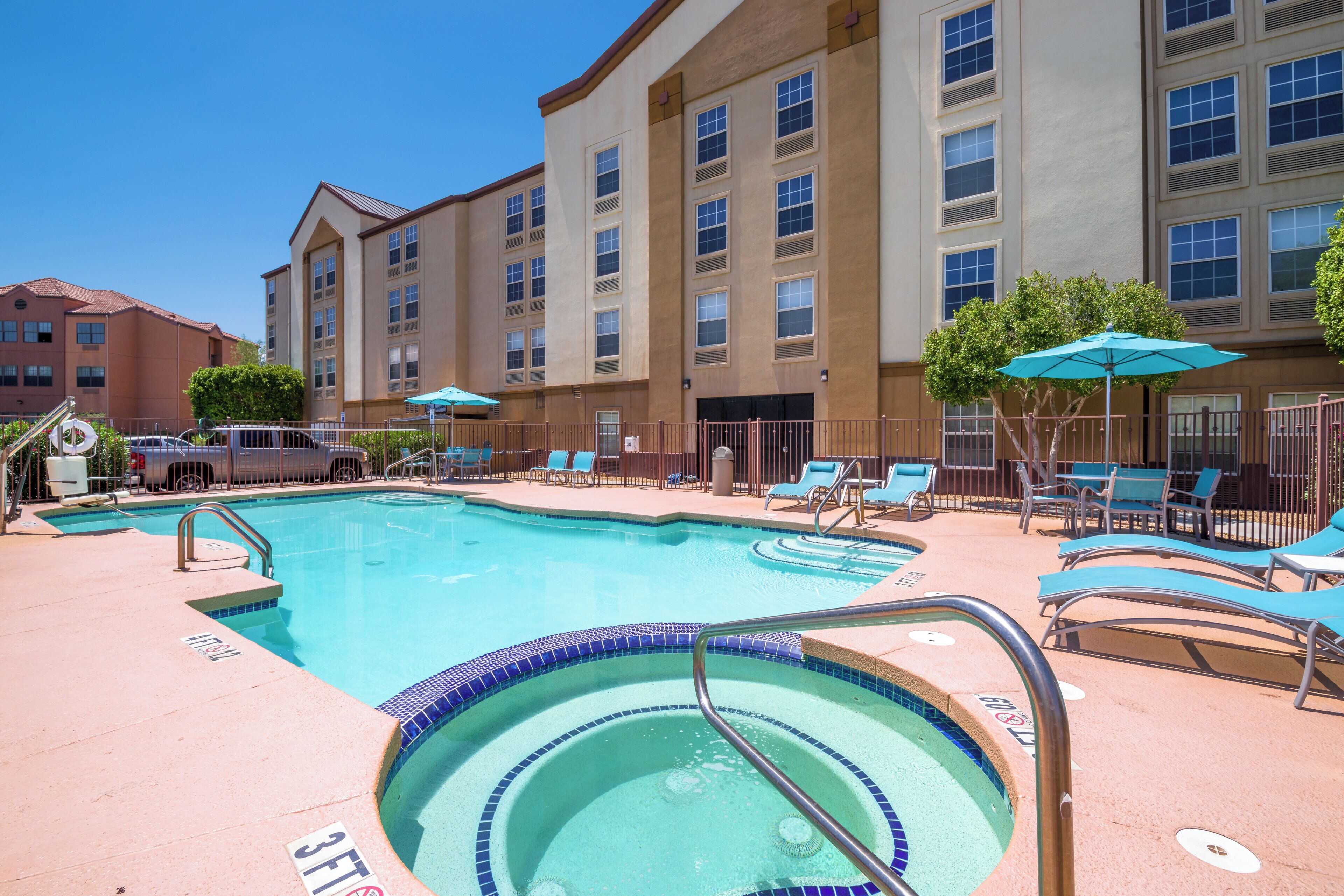 A hotel pool area with a large pool, lounge chairs, and umbrellas.