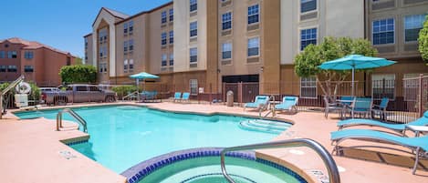 A hotel pool area with a large pool, lounge chairs, and umbrellas.