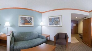 A hotel room with a green sofa, a wooden table, two lamps, and two framed abstract artworks on the walls. - Holiday Inn Express Hotel & Suites Phoenix-Airport by IHG (Phoenix)