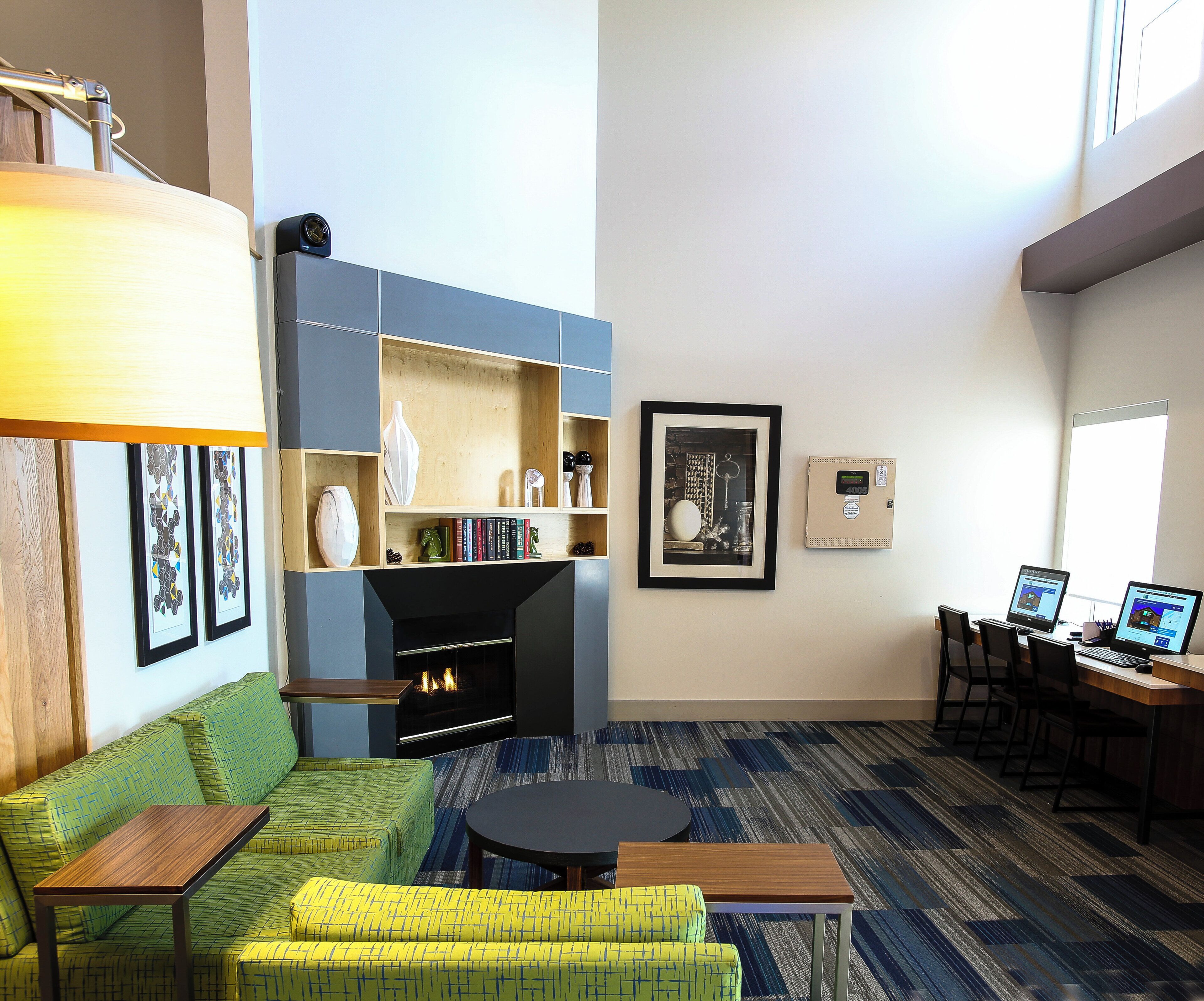 A modern living room with a fireplace, seating area, and a desk with two laptops.