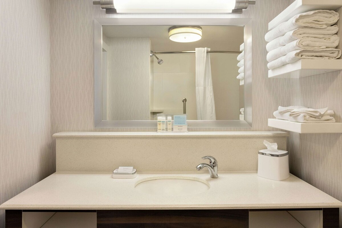A bathroom with a sink, mirror, towel rack, and a shower curtain.