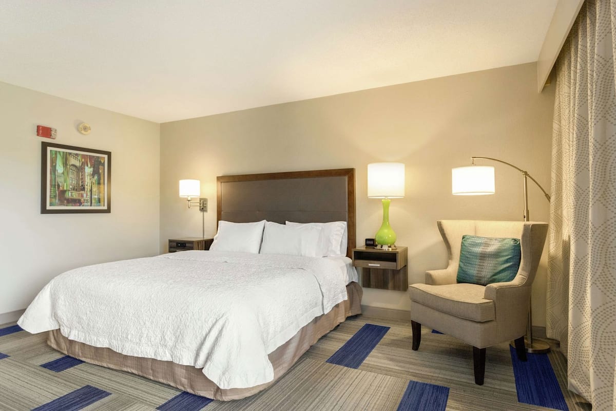 Een hotelkamer met een groot bed, een stoel, een nachtkastje, een lamp en een schilderij aan de muur.