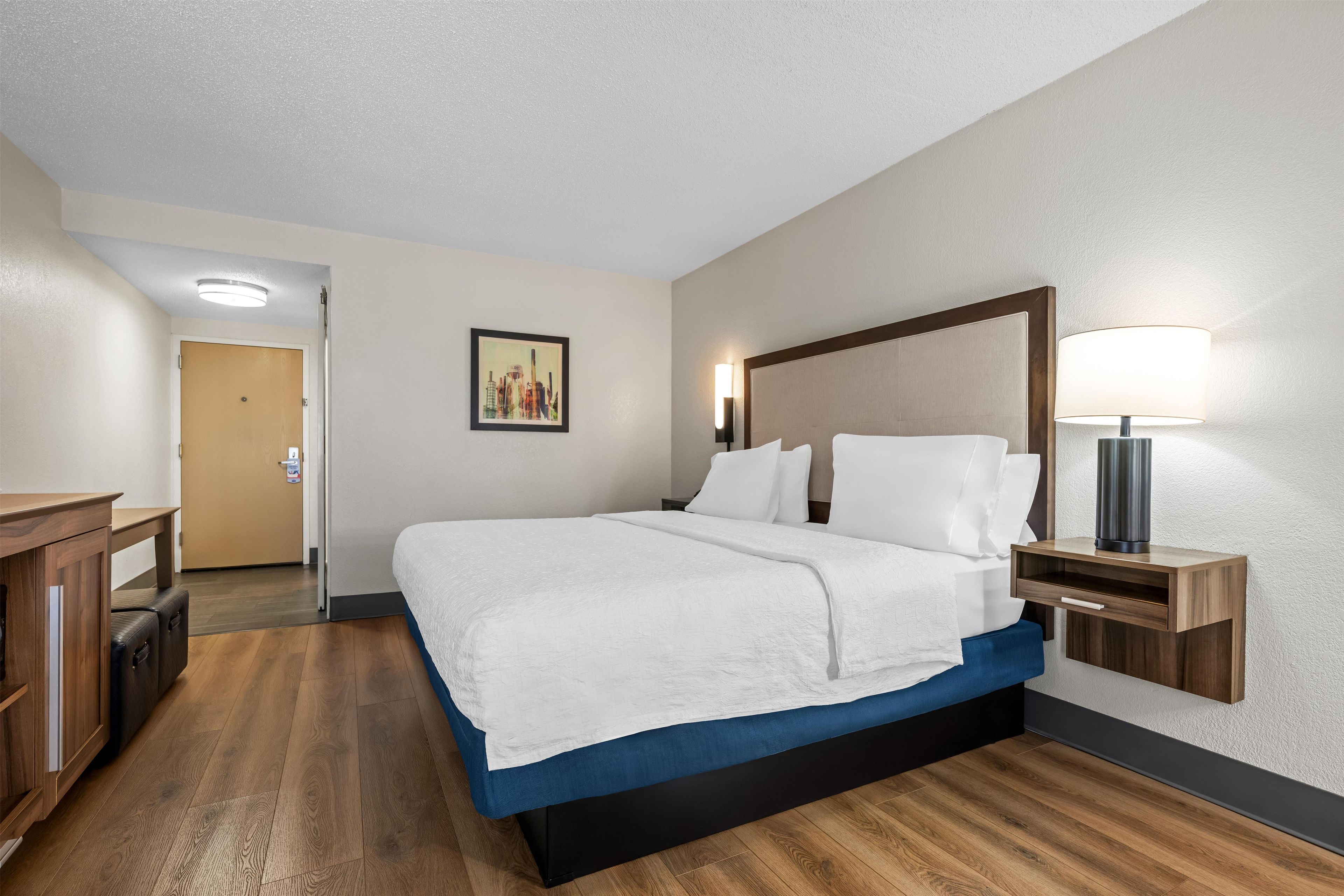 A hotel room with a bed, bedside tables, a desk, and a door.