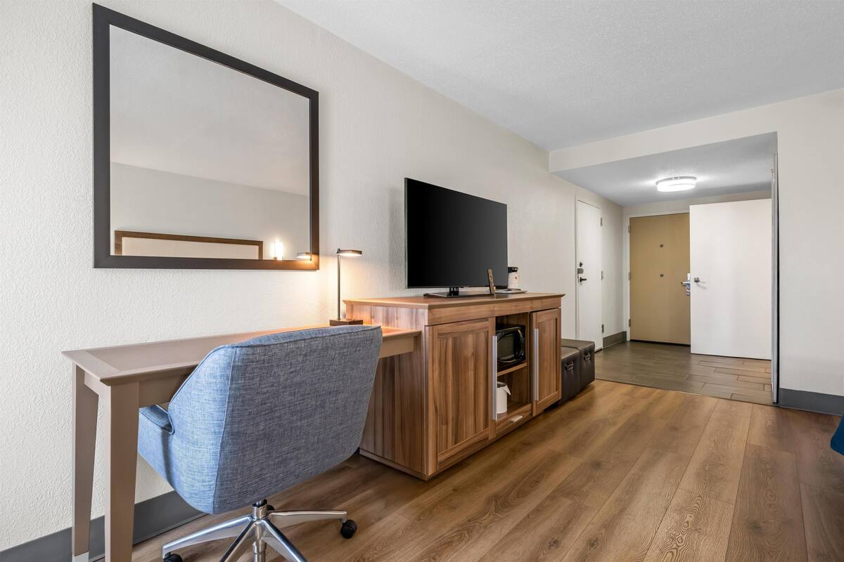 A hotel room with a wooden desk, a chair, a flat-screen TV, a microwave, and a door leading to another room.