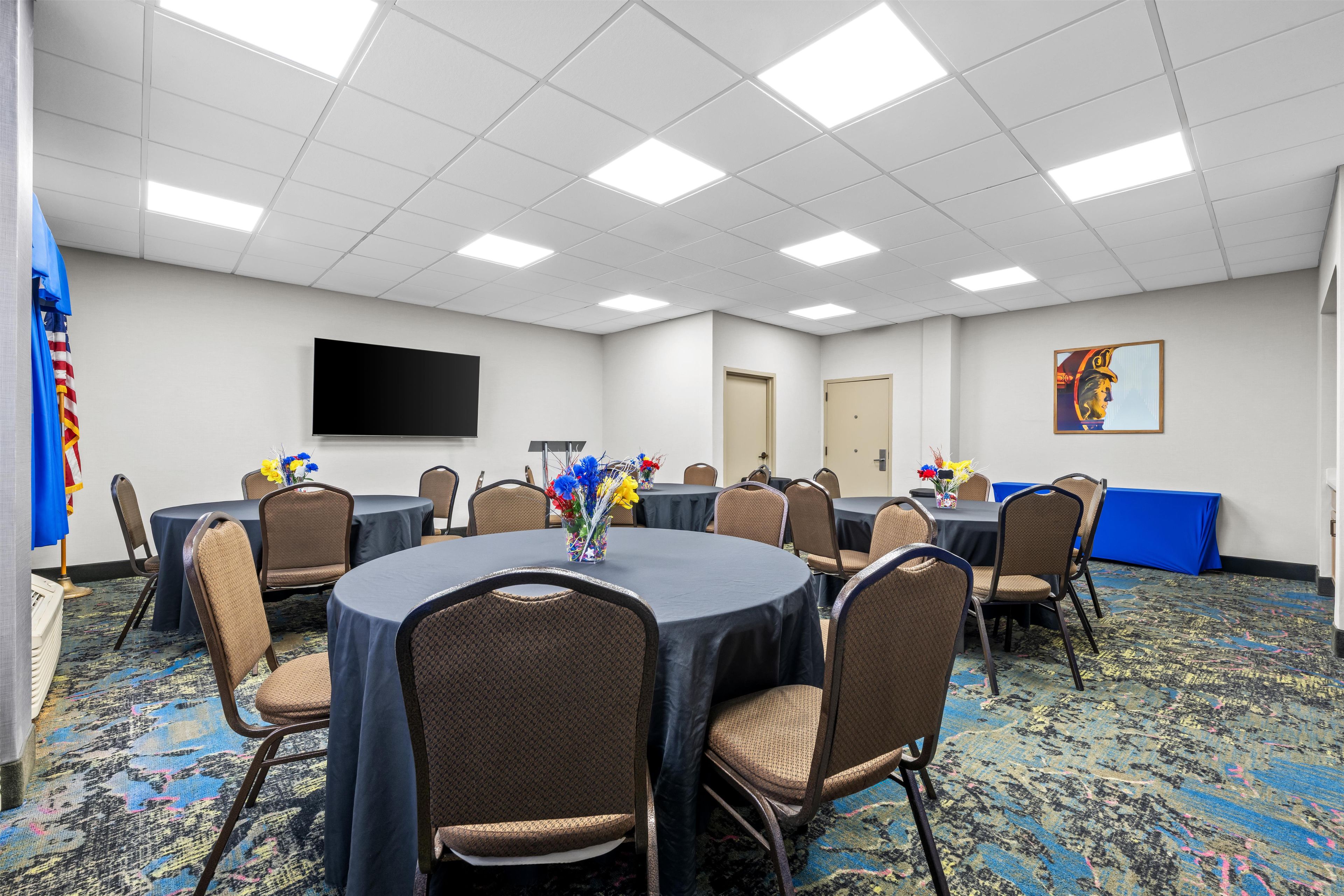 A conference room with round tables, chairs, a flat-screen TV, and a painting on the wall.