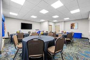 A conference room with round tables, chairs, a flat-screen TV, and a painting on the wall. - Hampton Inn Birmingham/Trussville (Birmingham)