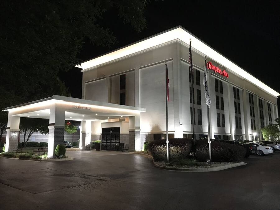 Entrada de hotel con un área techada, un letrero que dice "Welcome" y un asta con banderas.
