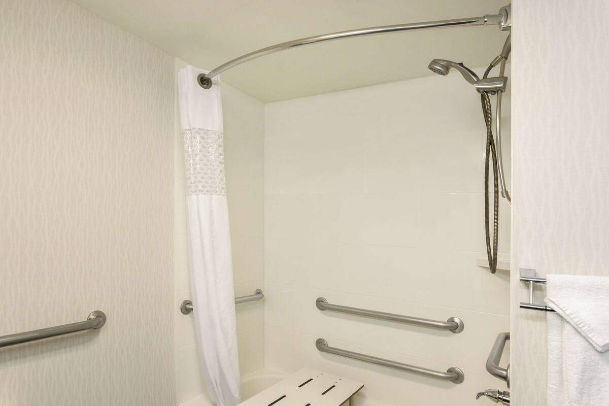 A shower area with grab bars, a showerhead, and a towel rack.