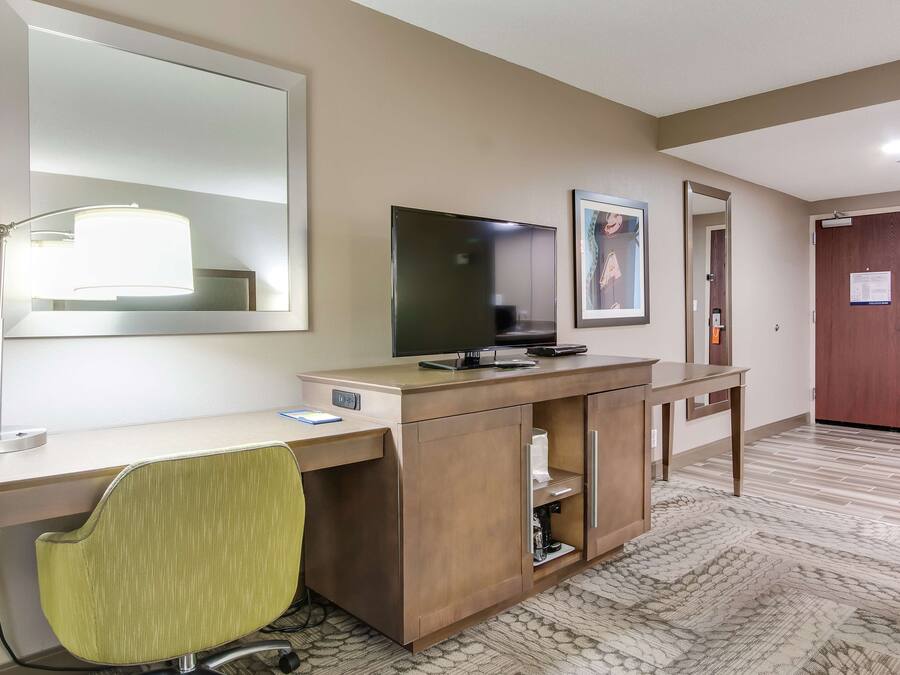 Habitación de hotel con escritorio, silla, televisor y un espejo grande.