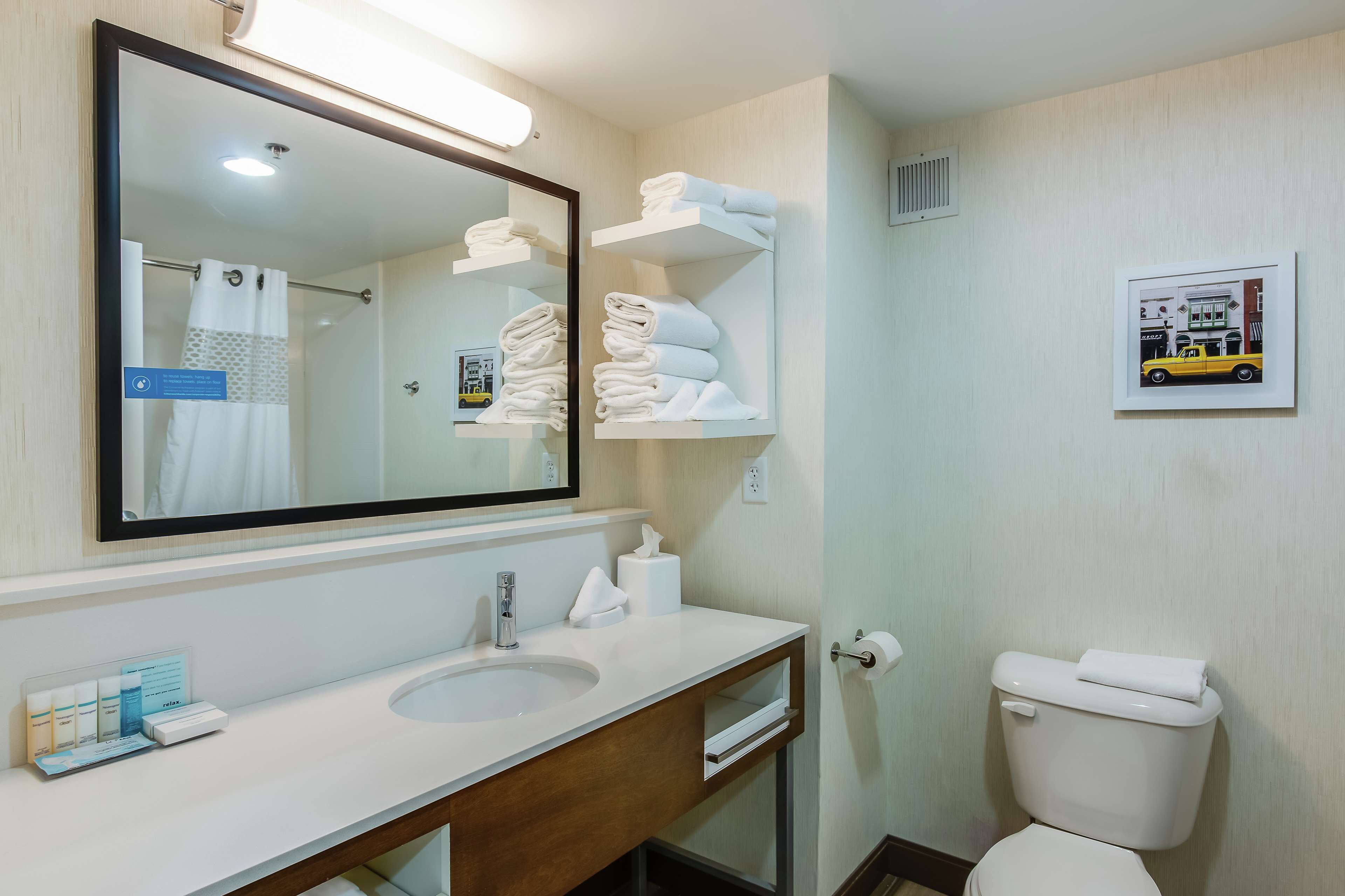 A modern bathroom with a large mirror, white sink, and neatly folded towels on shelves.