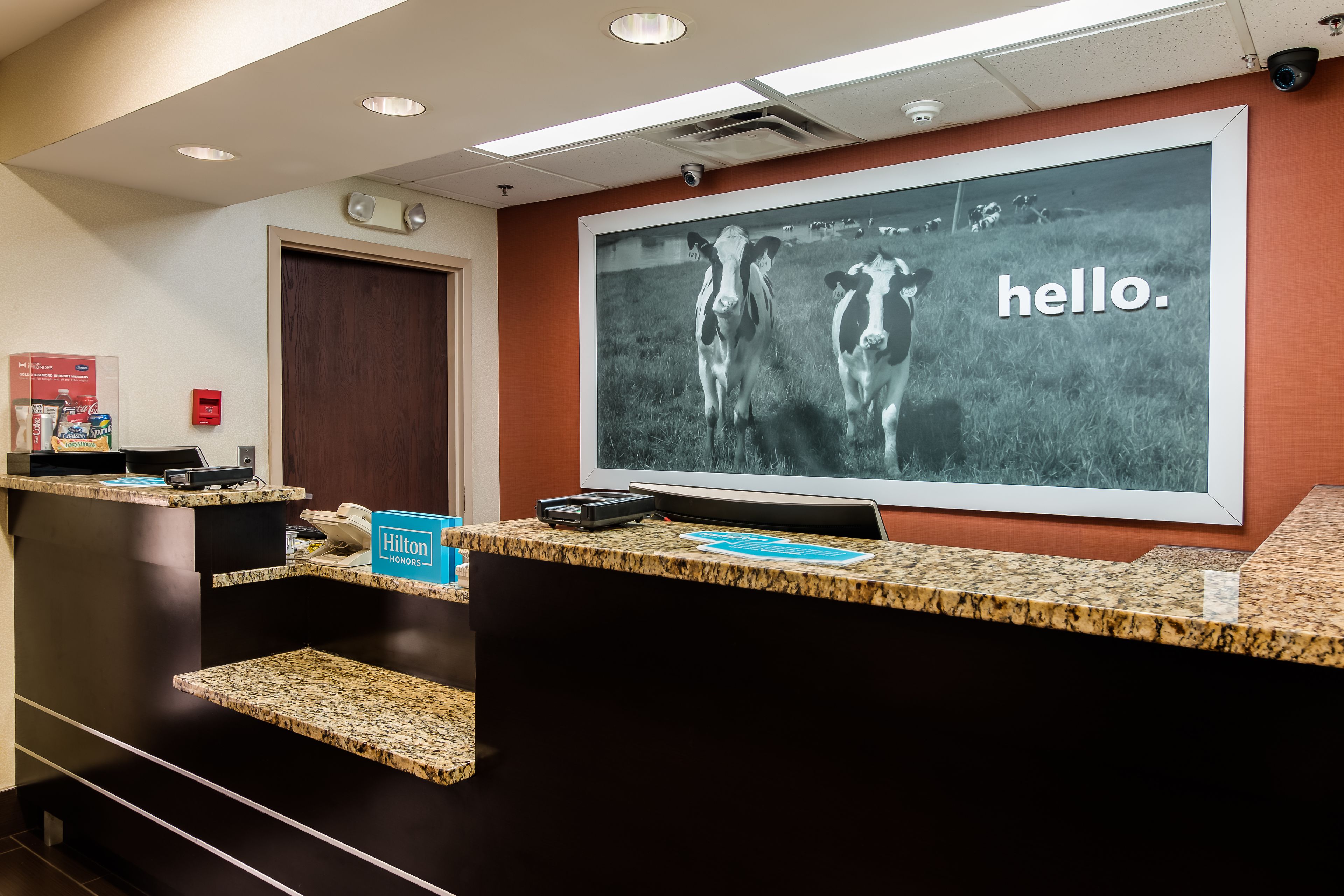A hotel reception area with a large framed picture of cows and the word "hello."
