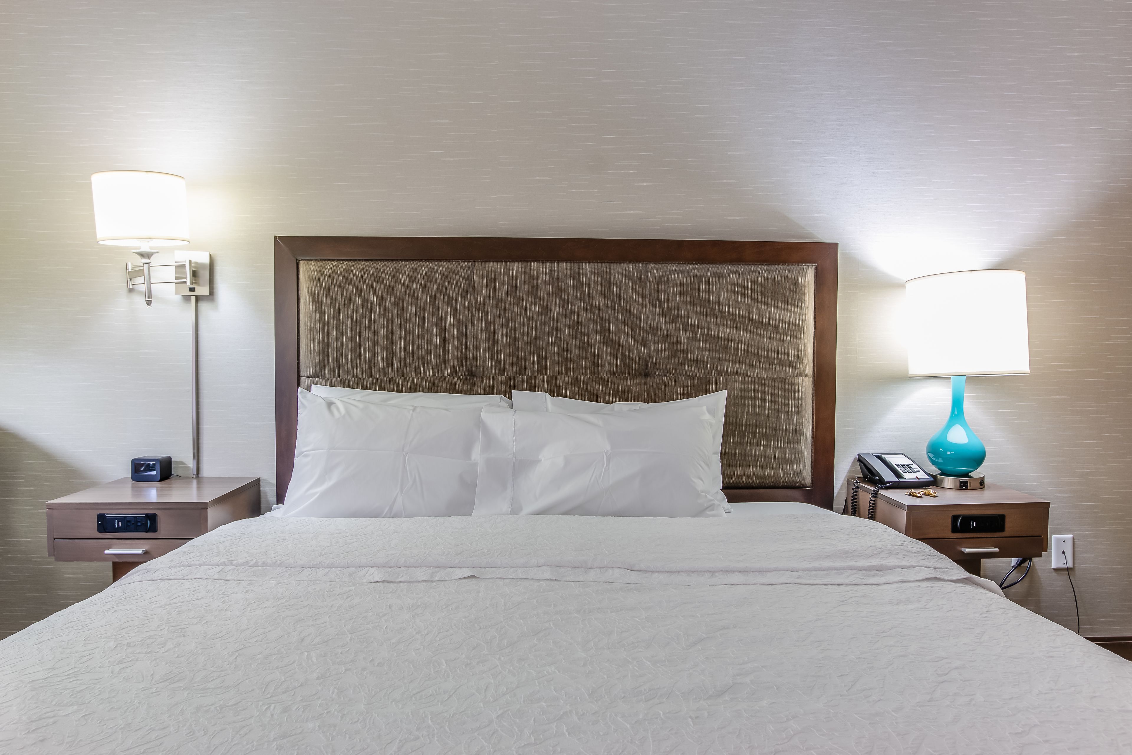 Una cama bien hecha con sábanas blancas, dos mesitas de noche con lámparas y un cabecero de madera.