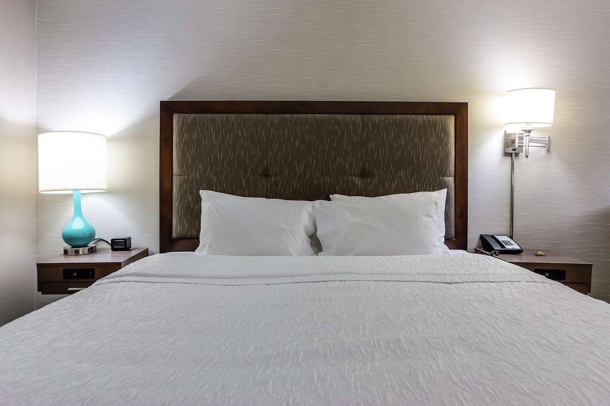 A neatly made bed with white linens, a wooden headboard, and two bedside tables with lamps and a phone.