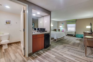 A hotel room with a bathroom, a bed, a desk, and a window.