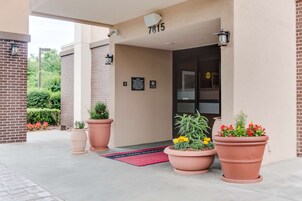 A hotel entrance with a number 7815 sign, large potted plants, and a red doormat.