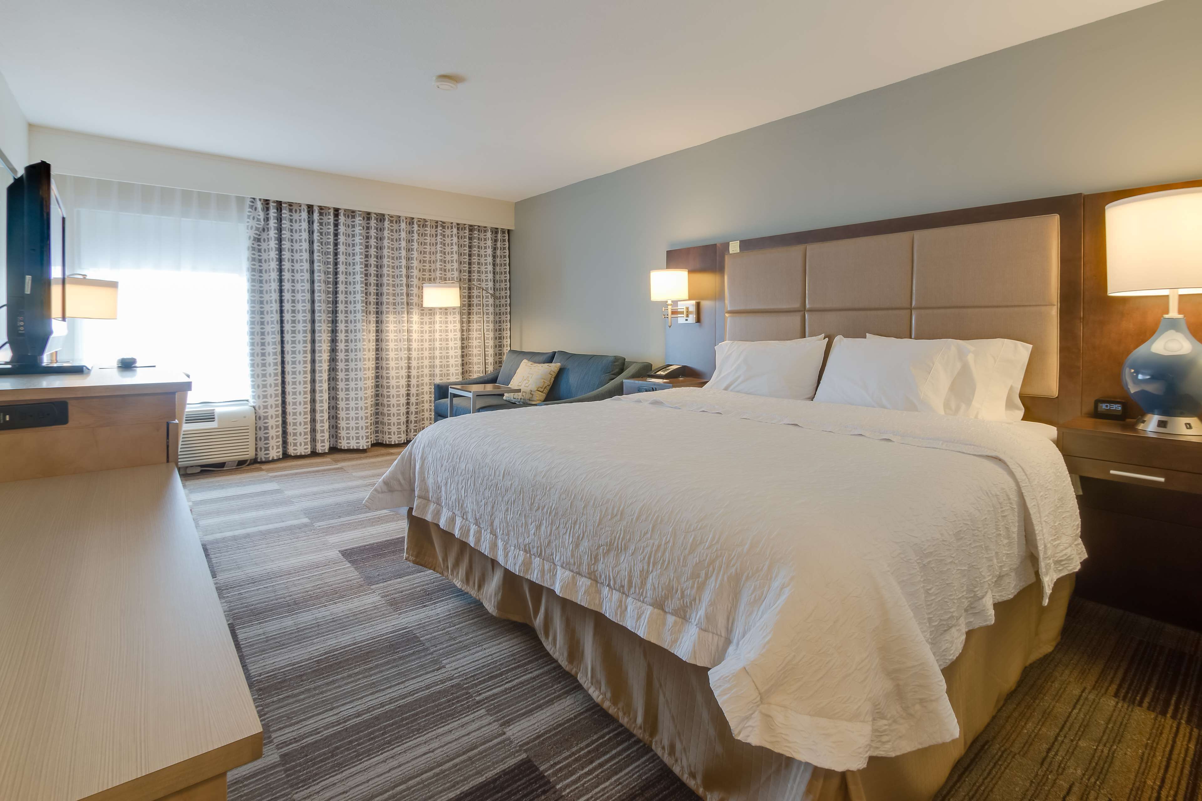 Ein Hotelzimmer mit einem großen Bett, einem Schreibtisch, einem Stuhl und einem Fernseher.