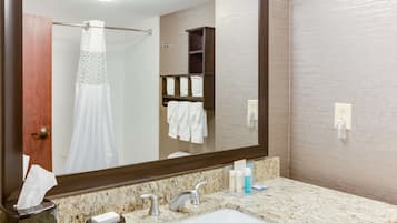 Un baño con un espejo grande, encimera de mármol, dos lavamanos, un perchero y una cortina de ducha.